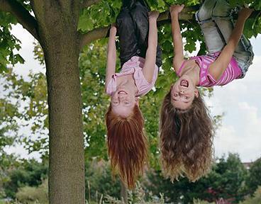 Two girls (8-10) hanging upside down in tree, smiling, portrait